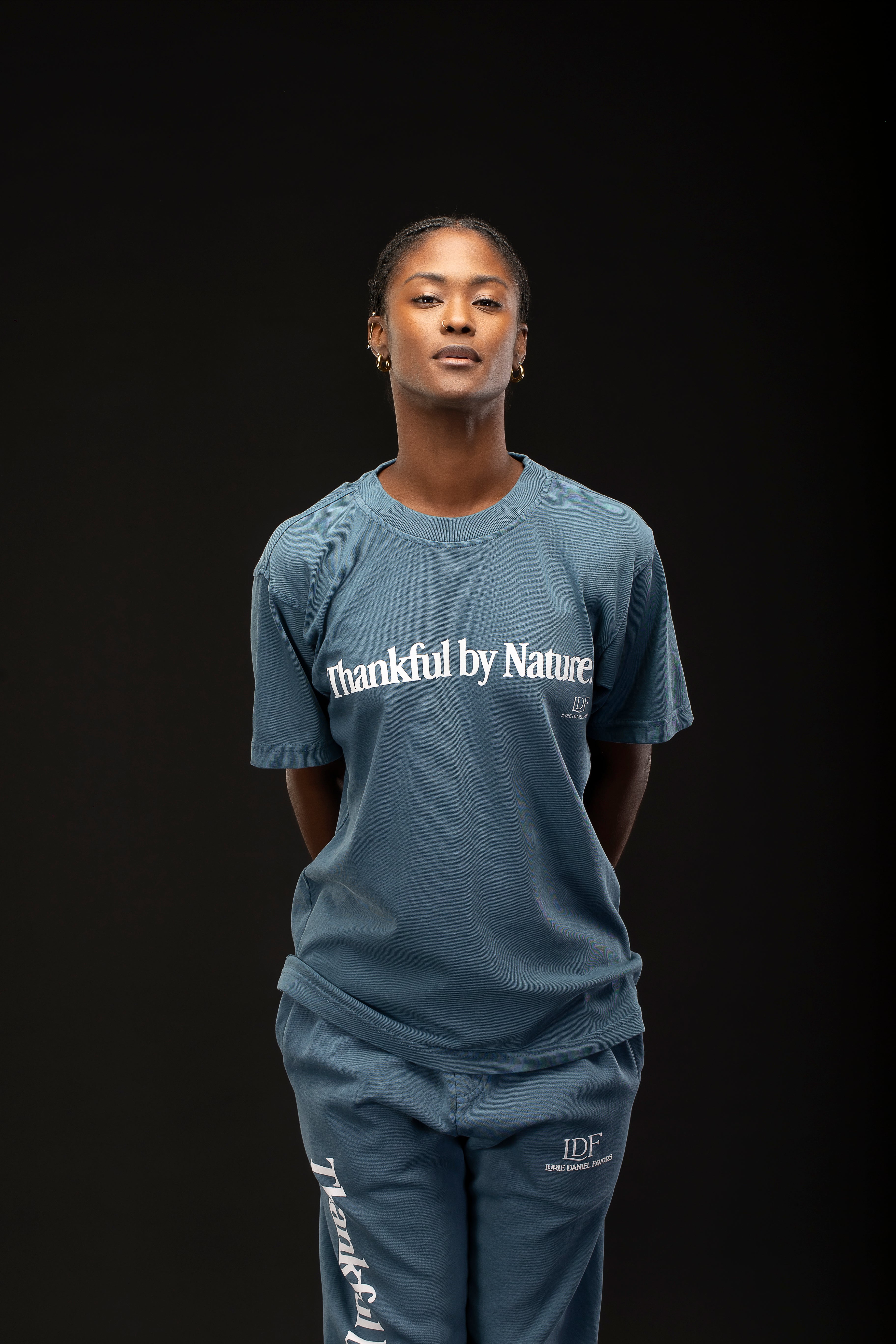 Woman wearing a blue 'Thankful by Nature' t-shirt on a black background