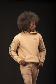 Man wearing a beige hoodie and pants with visible branding on a black background